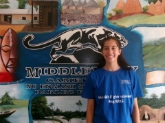 Student in blue shirt smiling in front of Cameroon mural